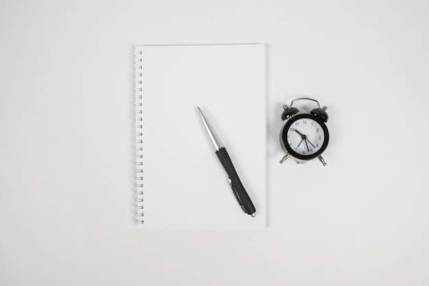 Top view of white notepad black alarm clock and pen on white background