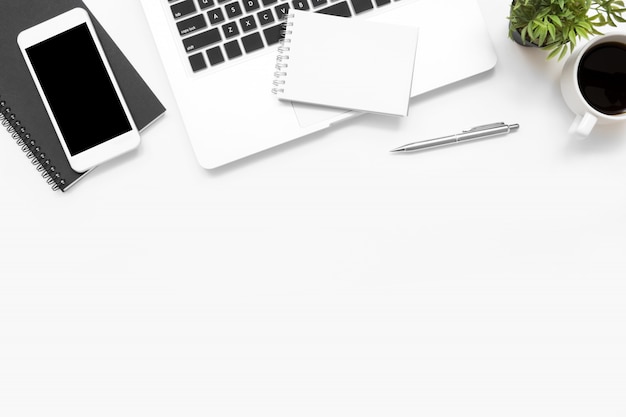 Top view of white office desk table with laptop computer, smartphone with blank screen and supplies.