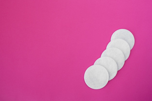 Top view on white round cotton disks laid out on a pink background