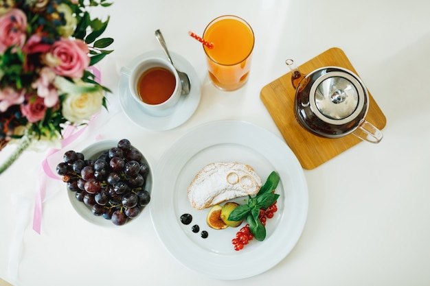 Top view of a white table with a glass teapot a cup of tea and a glass of juice white plate with a