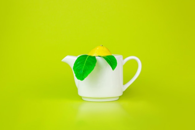 Top view of white teapot and tea leaves on green background. Refreshing Lemon Tea.