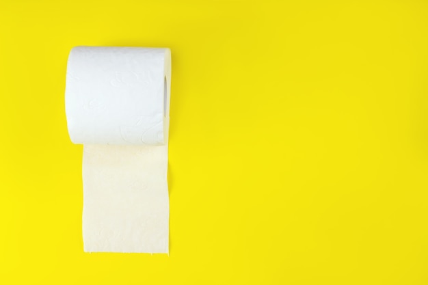 Top view of white toilet paper rolls on yellow background with copy space.