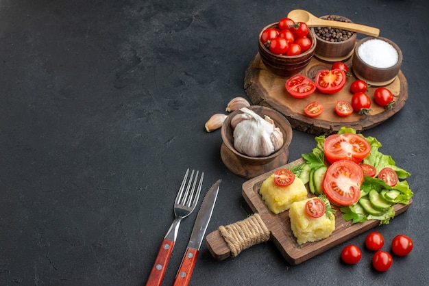 Top view of whole cut fresh vegetables and spices on wooden board white towel cutlery set cheese on the left side on black surface