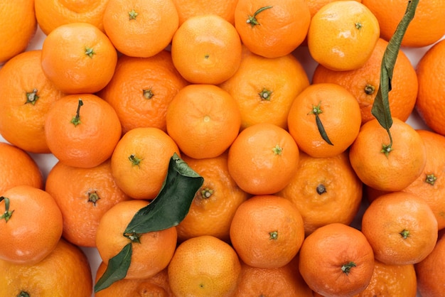 Top view of whole ripe tangerines with green leaves in stack on white background