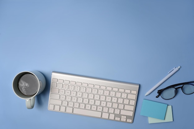 Top view wireless keyboard coffee cup and glasses on blue background