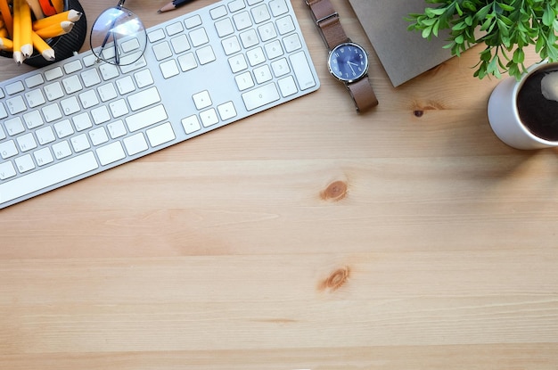 Top view wireless keyboard coffee cup glasses notebook and houseplant on wooden table