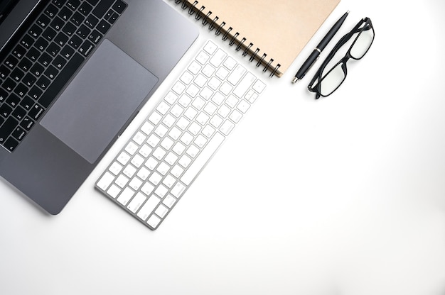 Top view with copy space of white table with laptop, keyboard, notebook, pen and glasses.Flat lay.