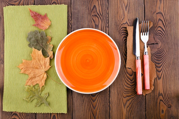 Top view with empty orange plate ready to place food cutlery colored leaves on rustic wooden table Autumn table with copy space