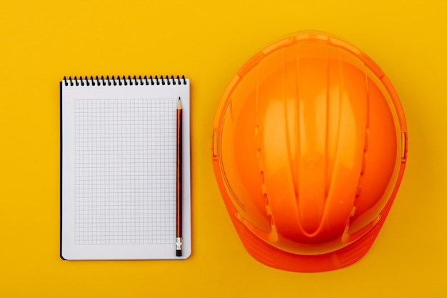 Top view with an orange safety engineer's helmet and an empty Notepad on a yellow background