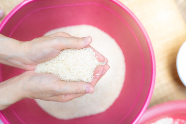 Top view woman hand holding rice above red plastic bowl Global food crisis Raw dry rice Uncooked