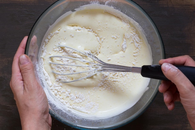 Top view of woman hand mixing with whisk dry ingredients and batter on wooden background