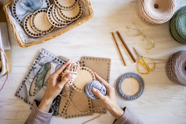 Photo top view woman hands knitted accessory interior decor use ribbon yarn and wooden stencil pattern on desk table at home closeup female arms creating exclusive handmade craft details art work