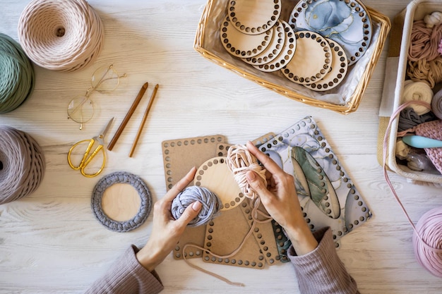 Photo top view woman hands knitted accessory interior decor use ribbon yarn and wooden stencil pattern on desk table at home closeup female arms creating exclusive handmade craft details art work