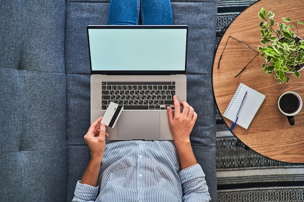 Top view of woman holding a credit card and shopping online at a computer.