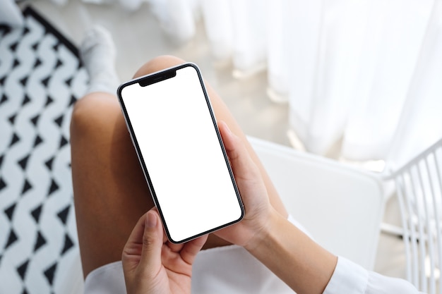 Top view  of woman holding mobile phone with blank desktop white screen while sitting in bedroom with feeling relaxed