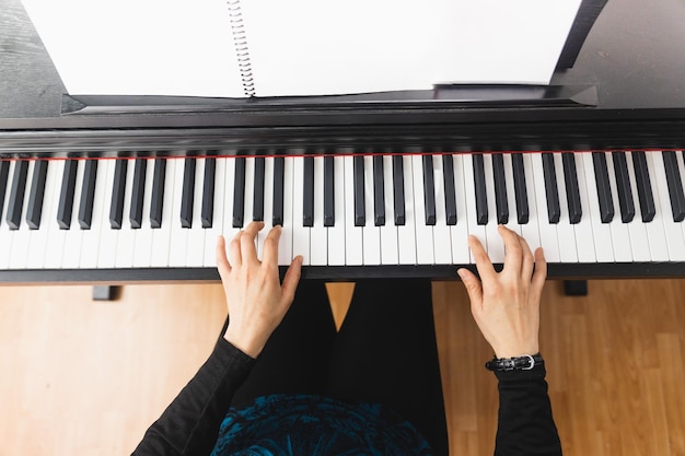 Top view of woman's hands playing piano by reading sheet music.