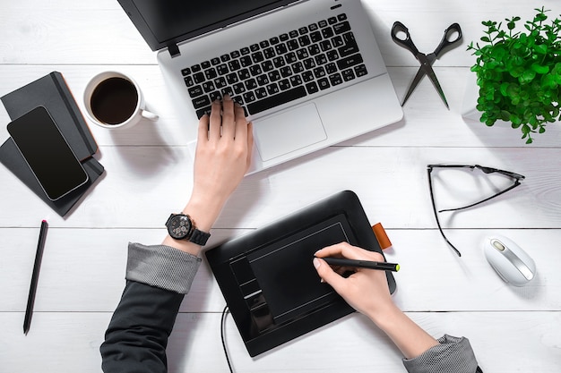 Top view of woman's hands typing on laptop keypad placed on white office desktop with coffee cup.