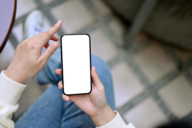 Top view of a woman sits at the backyard and uses her smartphone phone white screen mockup