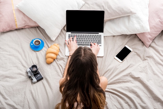 Top view on the woman working with laptop on the bed