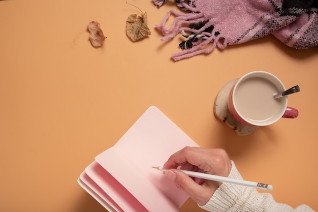 Top view of woman writing on blank notebook Female hand writing on empty notepad with coffee cup plaid on colored background