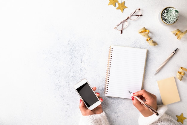 Top view of woman writing on notepad while holding smartphone