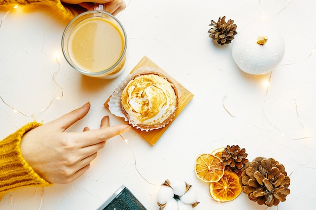 Top view of womens hands touching coffee mug and tartlet girl in knitted sweater is having breakfast...