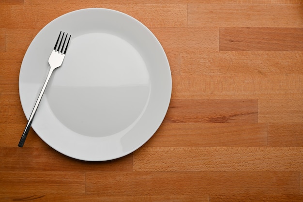 Top view of wooden dinning table with mock up ceramic plate fork and copy space