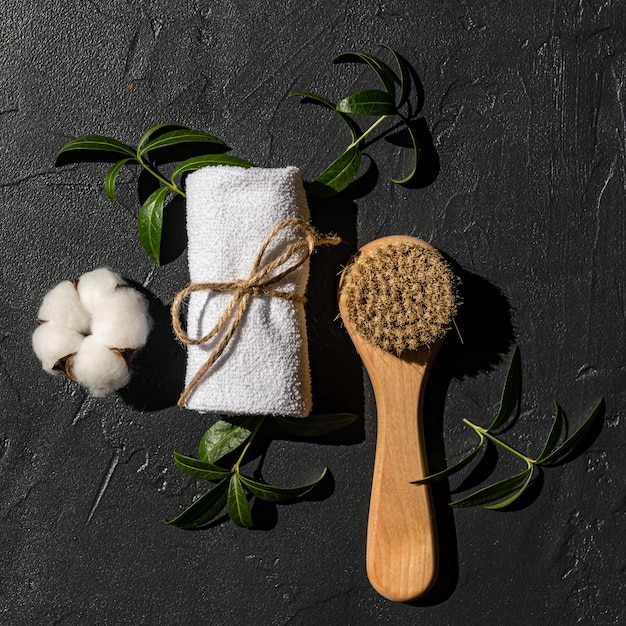 Top view of wooden massaging brush with natural bristle and white rolled towel ready for home spa procedures. Personal accessories