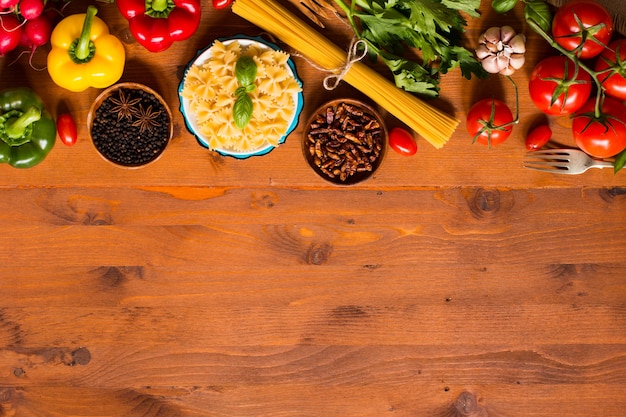 Top view of a wooden table full of italian pasta ingredients like peppers, tomatoes, olive oil, basi