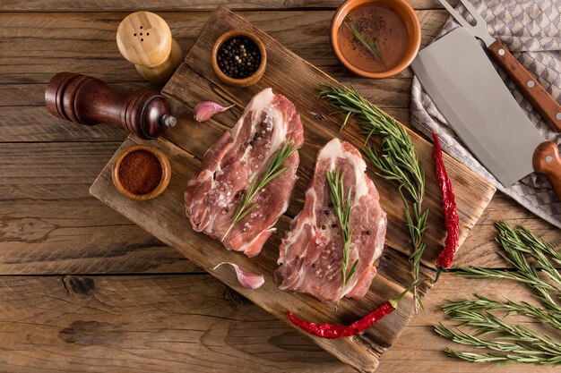 Photo top view of a wooden table with barbecued pork steaks from farmer meat spices for cooking on a wooden board