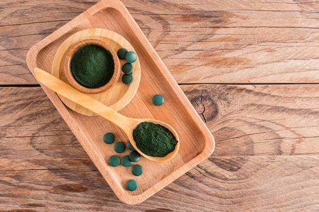 Photo top view of the wooden table with environmentally friendly dishes filled with spirulina algae powder and green tablets food additive