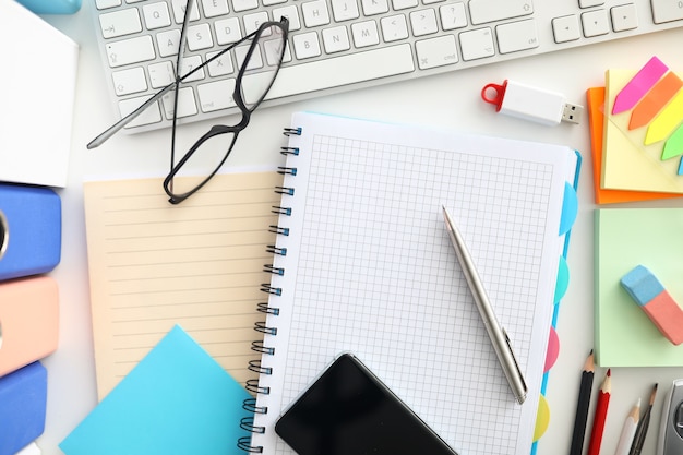 Top view of working place. Open notebook and silver pen. Black glasses. White modern keyboard on desktop. Details for work. Office stationery and creativity concept