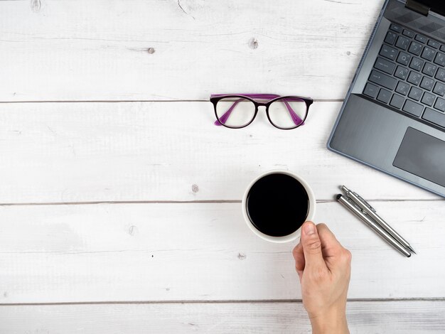 Top view workspace laptop glasses and two silver pen and hand hold coffee cup copy space