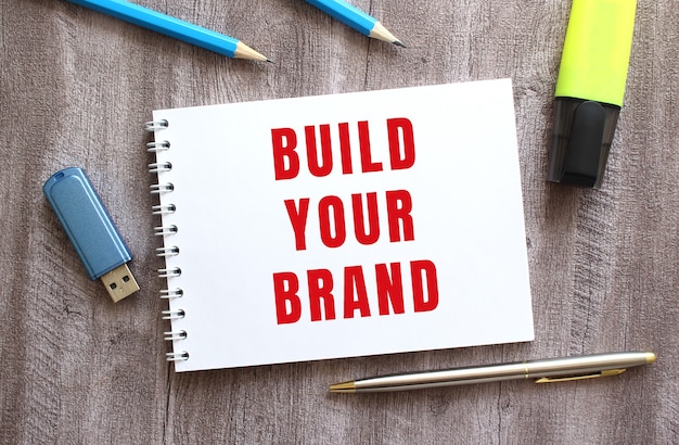 Top view of the workspace notepad with build your brand text pen pencils flash drive on gray wooden