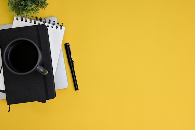 Top view workspace with coffee cup pen notepad and copy space on yellow background