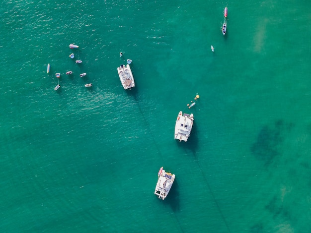 Top view of yacht sailing with jet ski and banana boat on turquoise tropical sea