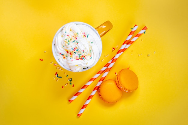 Top view of yellow coffee cup, straws and french macaroons on yellow