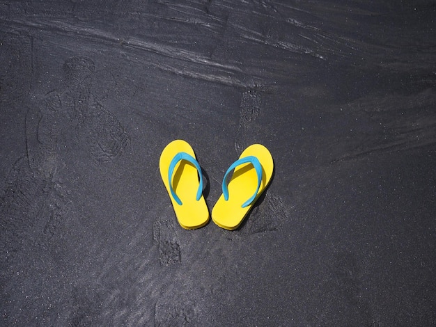 Top view of yellow sandal on black sand summer beach background Holiday vacations concept