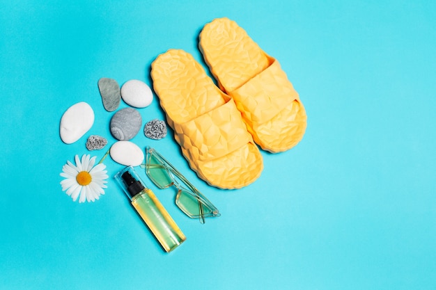 top view of yellow slippers, sunglasses and oil tube decorated with chamomile flower and pebbles