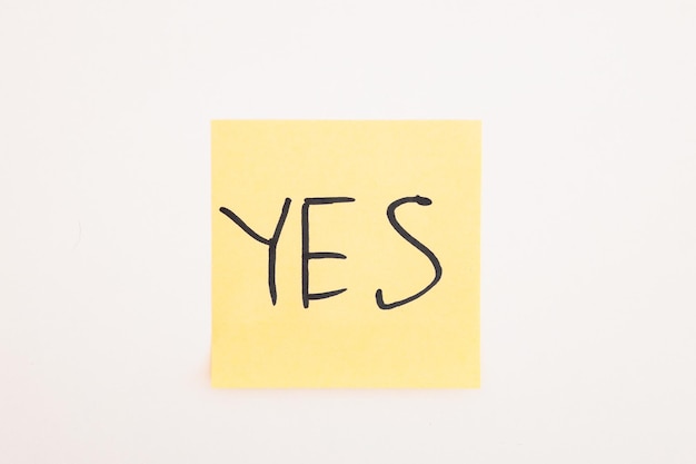 Top view of yellow stick note with yes lettering on white background