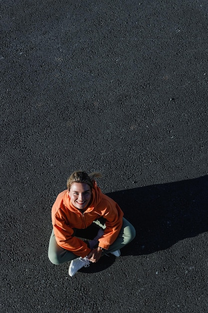 Top view of a young adult woman wearing activewear sitting on the asphalt