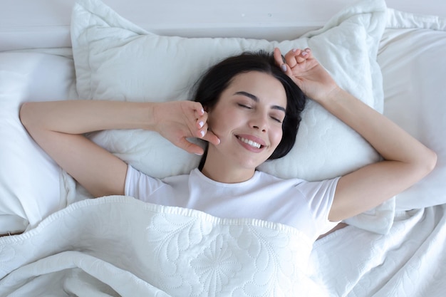 Top view young beautiful brunette woman sleeping in bed with eyes closed smiling in sleep wearing