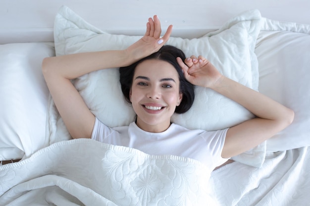 Top view young beautiful woman sleepy in morning smiling and looking at camera lying in bed with