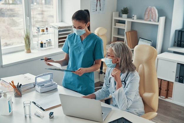 Top view of young female nurse in protective mask talking to mature doctor while working in the hospital