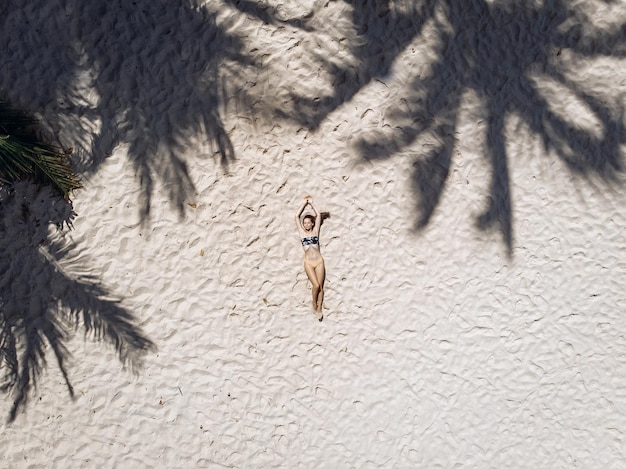 Top view of a young girl with a perfectly slim body lying on the golden sand on the beach