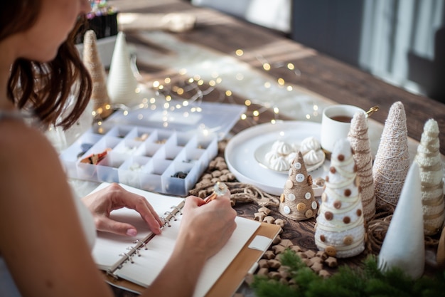 Top view of young woman is writing goals for new year  on diary on desk with christmas tree