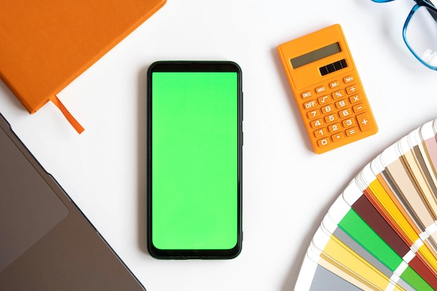 Top view of zoom Mobile Phone Green Screen on Designer Worktop Close Up Color Guide Palette Laptop Pen Cell Phone Mockup with Blank Chromakey Display on a Workplace Smartphone Layout Color key