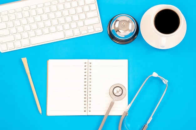 Top viwe of modern workplace with stethoscope and keyboard on blue table background. 