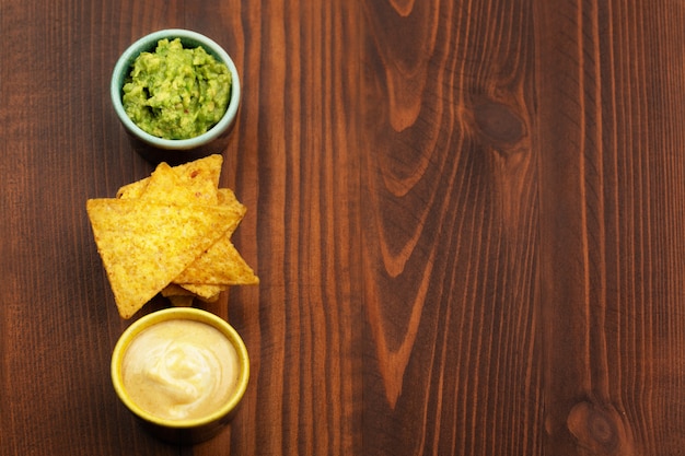 Tortilla chips nachos, sauce guacamole and cheese sauce on wooden background. Space for text