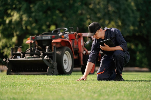 Photo touching the grass man is with utility tractor with grass cutter and aerator equipment on the field